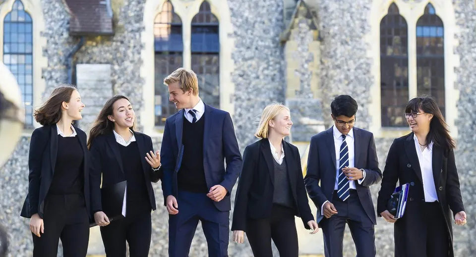 Un gruppo di studenti del Lancing College cammina davanti a un edificio storico in pietra con finestre ad arco.