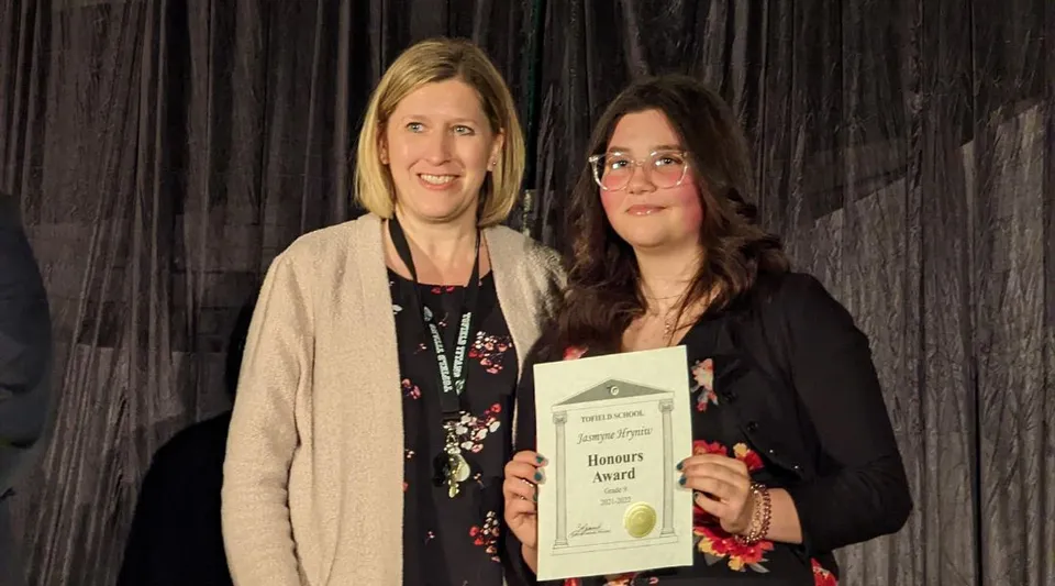 Due donne sono in piedi insieme e tengono un certificato nel campus della Tofield School.