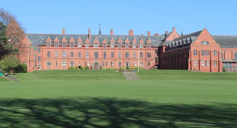 Il grande edificio in mattoni a vista con torri e comignoli nel campus dell'Ellesmere College sorge su un prato verde sotto un cielo limpido.