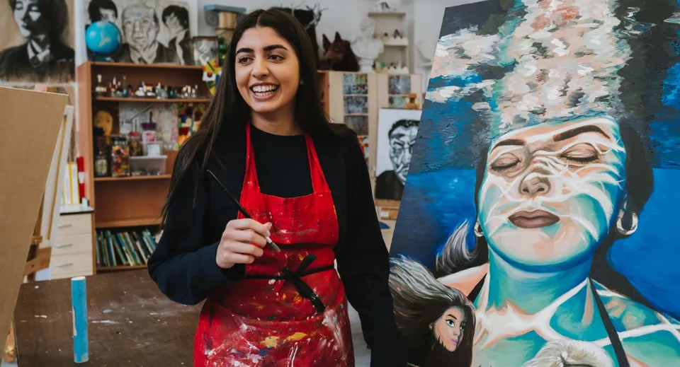 Una studentessa della Stamford High School è in piedi davanti a un'aula d'arte con molte opere d'arte e scaffali.