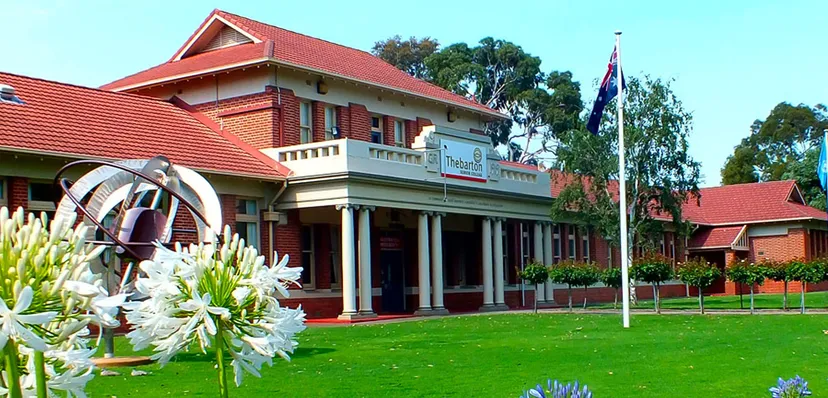 L'edificio a più piani del Thebarton Senior College con tetto rosso e colonne si trova su un prato con alberi e fiori in primo piano.