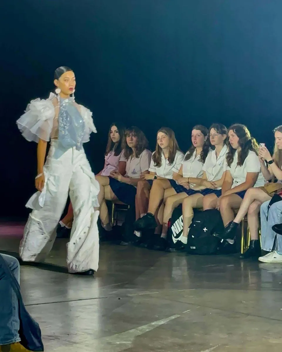 Una studentessa della Riverside Girls High School sfila sulla passerella con un abito bianco davanti alle compagne.