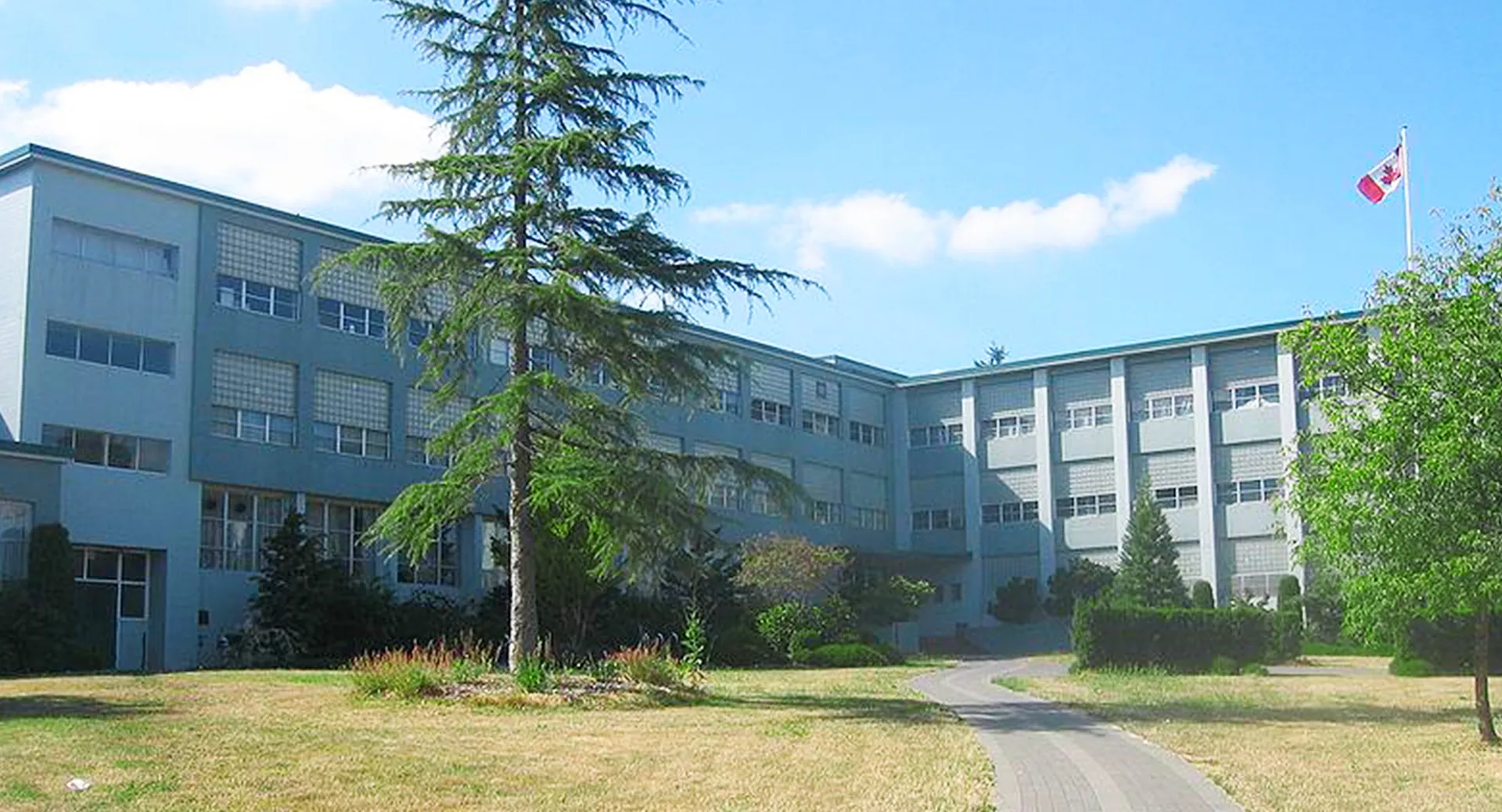 L'edificio scolastico a più piani della Sir Winston Churchill Secondary School è circondato da alberi e da un prato e mostra una bandiera canadese.
