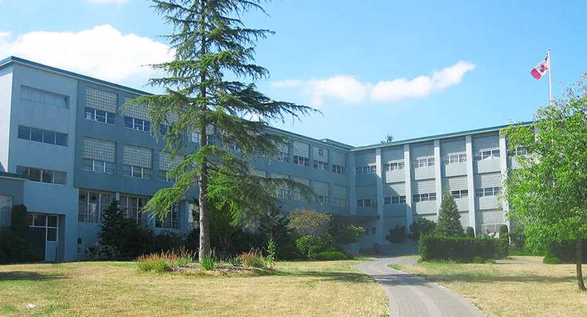 L'edificio scolastico a più piani della Sir Winston Churchill Secondary School è circondato da alberi e da un prato e mostra una bandiera canadese.