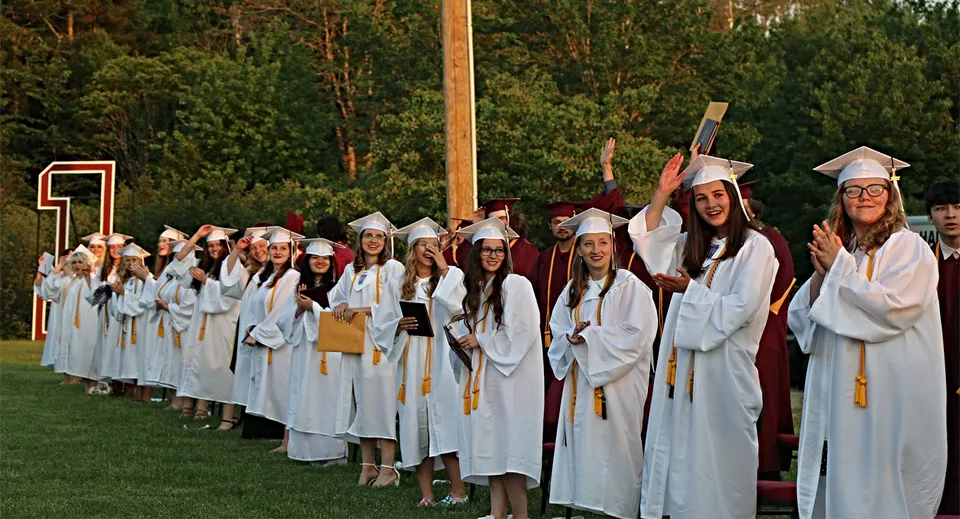 Un gruppo di diplomati in toga e tocco bianchi si trova davanti a un bosco nel campus della Washington Academy.