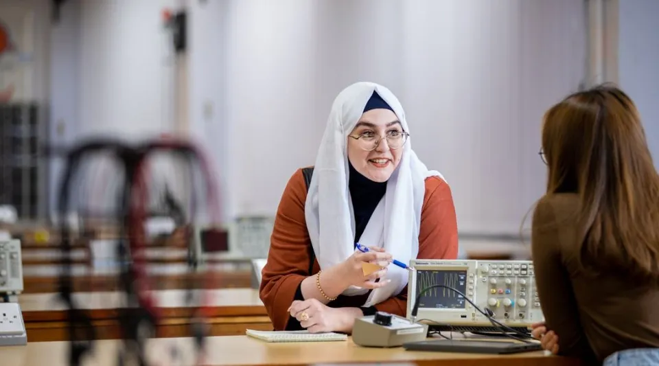 Una donna con l'hijab si trova a un bancone della reception e parla con una persona nel campus del National Mathematics and Science College.