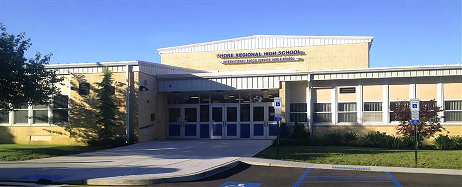 L'edificio moderno della Shore Regional High School con l'ingresso principale davanti a un cielo azzurro terso.