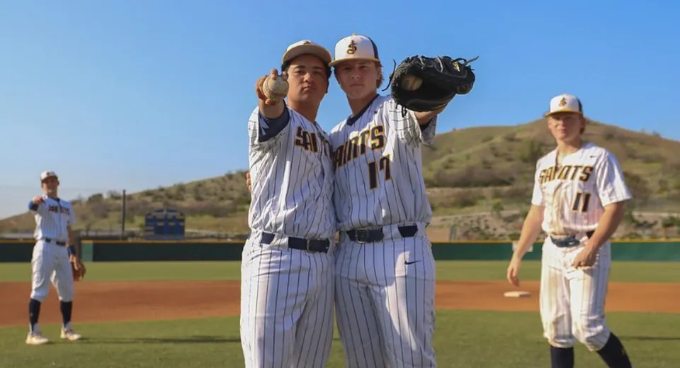 Un gruppo di giocatori di baseball della Crean Lutheran High School in divisa sul campo da baseball davanti a un cielo blu e alle montagne.