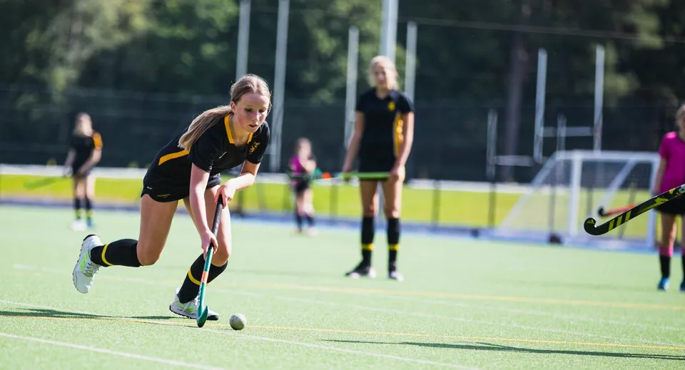 Una giocatrice di hockey della Wellington School guida la palla su un campo in erba sintetica.