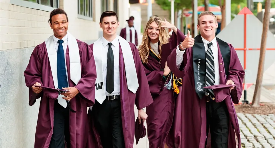 Quattro diplomati del Davis School District in toga rossa camminano insieme su un viale lastricato nel campus scolastico.