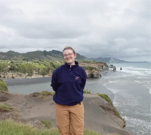 Carla lächelt auf einer Klippe mit Blick auf die Ozeanküste in Neuseeland