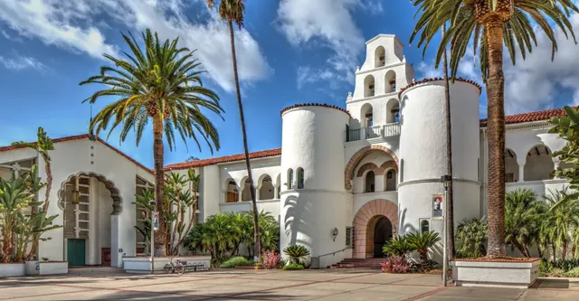 L'edificio bianco con torre campanaria della San Diego State University è circondato da palme e verde sotto un cielo azzurro.