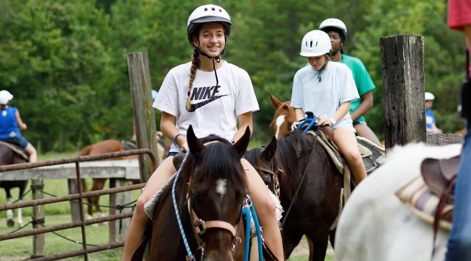 Due persone con il casco vanno a cavallo in un'area esterna recintata nel campus della Winston Salem Christian School.