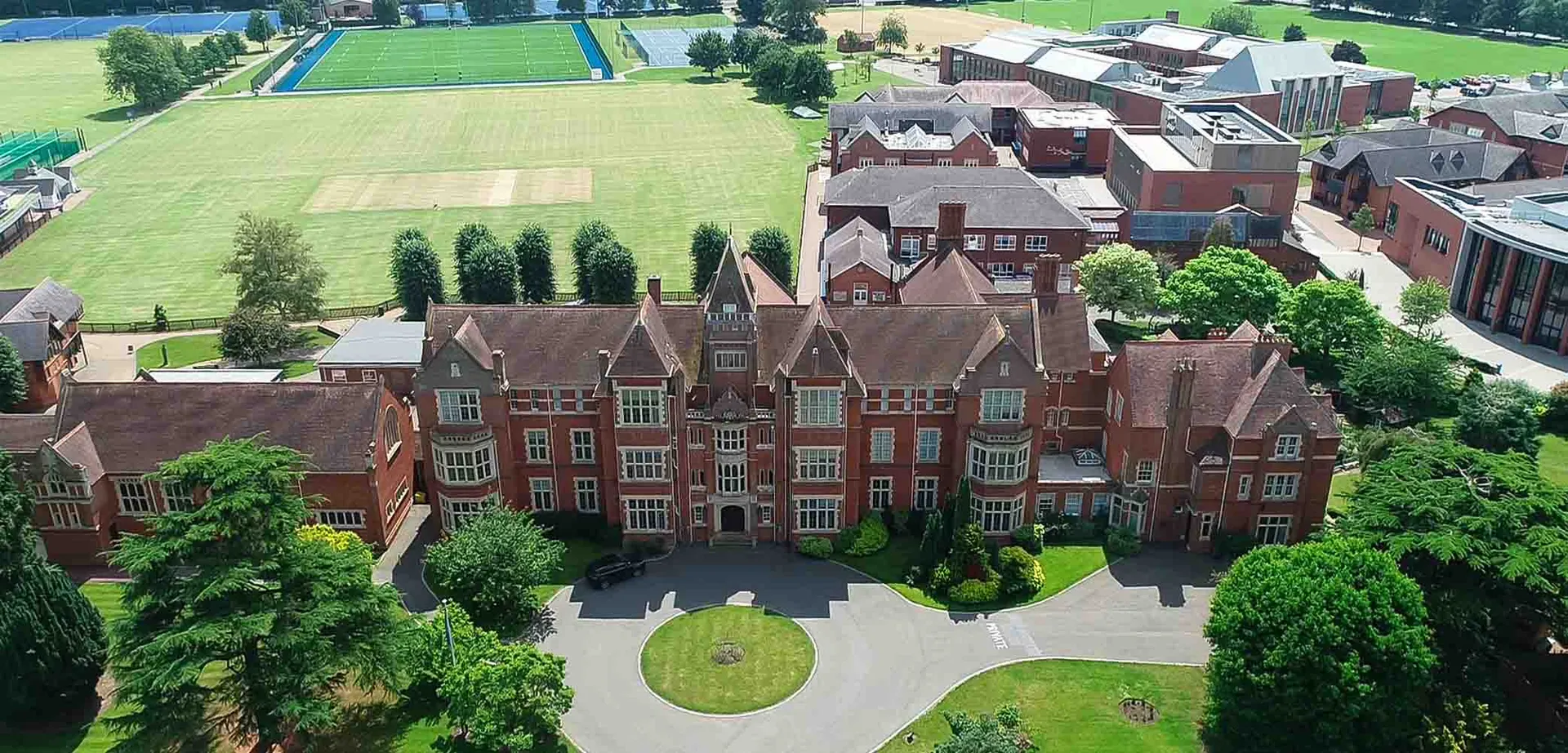 L'edificio storico in mattoni della Warwick School si trova in primo piano, circondato da un prato verde e alberi.