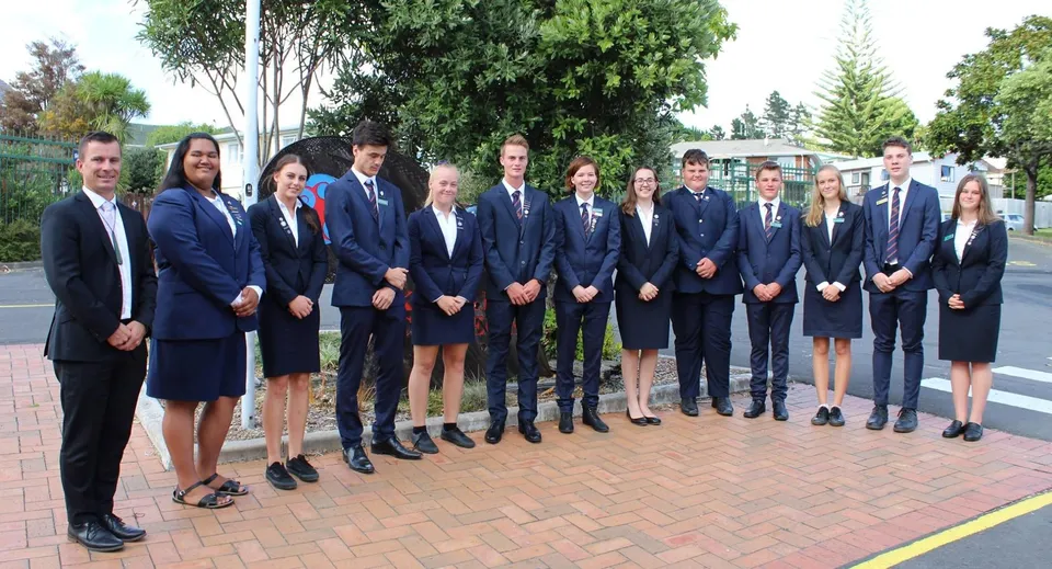 Un gruppo di studenti e studentesse del Kaipara College si trova in un'area esterna pavimentata circondata da alberi.