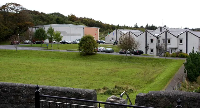 Un campo verde davanti a edifici residenziali e a un edificio industriale più grande nel campus del Rice College.