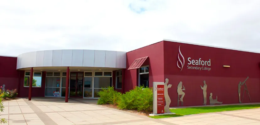 L'edificio moderno di colore rosso con il logo del Seaford Secondary College sorge su un terreno erboso sotto un cielo nuvoloso.