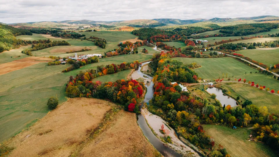 Una vista aerea del paesaggio autunnale nei pressi della Sussex Christian School con un fiume, campi e alberi colorati.