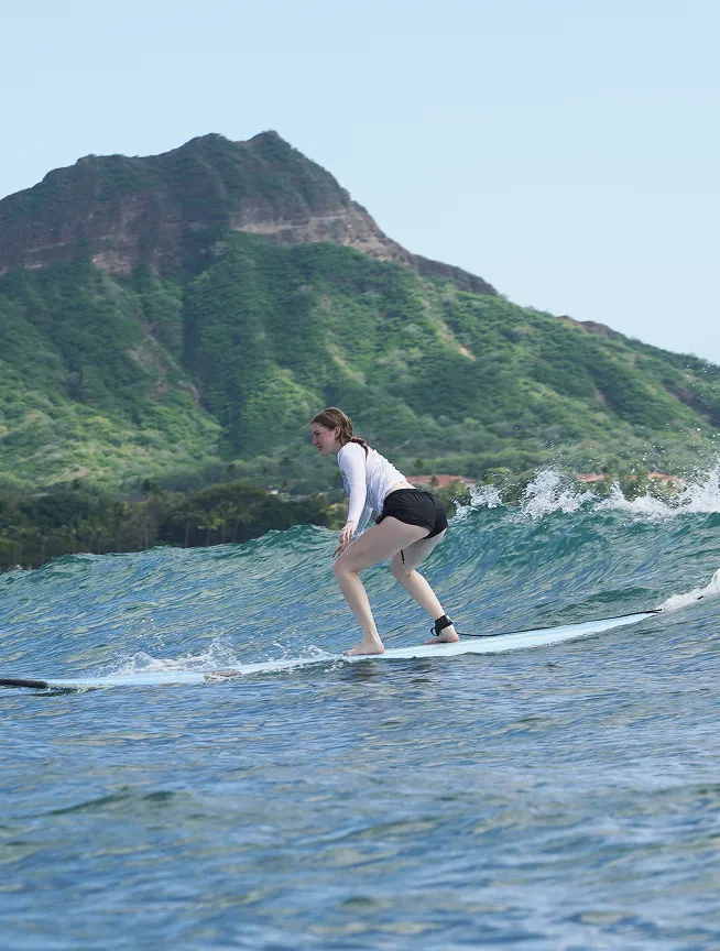 Estudiante haciendo surf sobre una ola con una montaña verde al fondo
