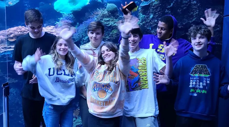 Un gruppo di studenti della Faith Christian School posa davanti a un'immagine sottomarina con coralli variopinti e creature marine.