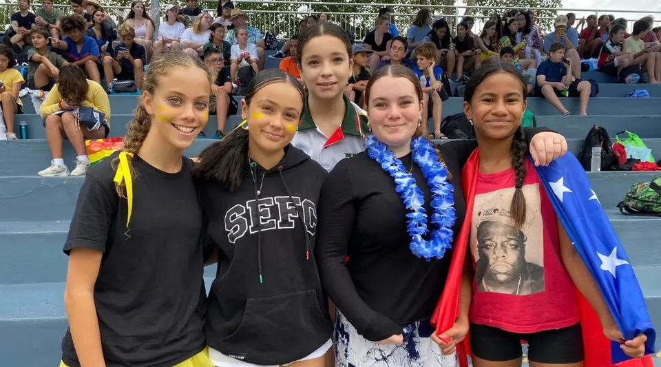 Un gruppo di giovani studentesse posa insieme nel campus della South Sydney High School con una grande folla sullo sfondo.