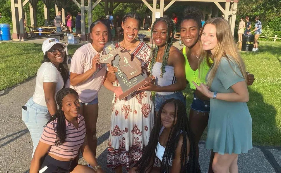 Studentesse della Huron High School tengono insieme una coppa all'aperto, davanti a edifici e alberi.