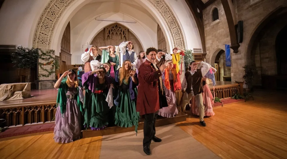 Un gruppo di studenti della Central Methodist University sta in piedi in costumi sgargianti all'interno di un ambiente finemente decorato con soffitti a volta.