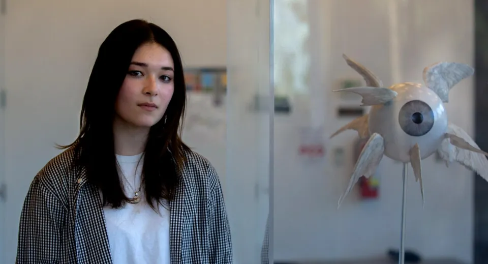 Una studentessa della Idyllwild Arts Academy di fianco a una scultura a forma di occhio con ali.