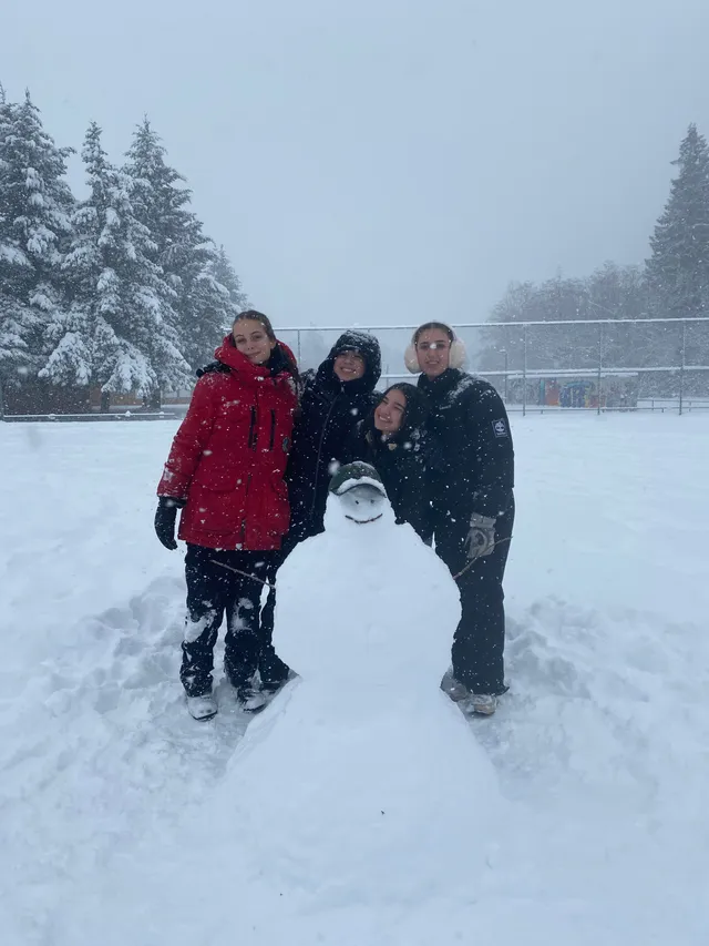 Cuatro chicas junto a un muñeco de nieve mientras nieva en el patio del colegio