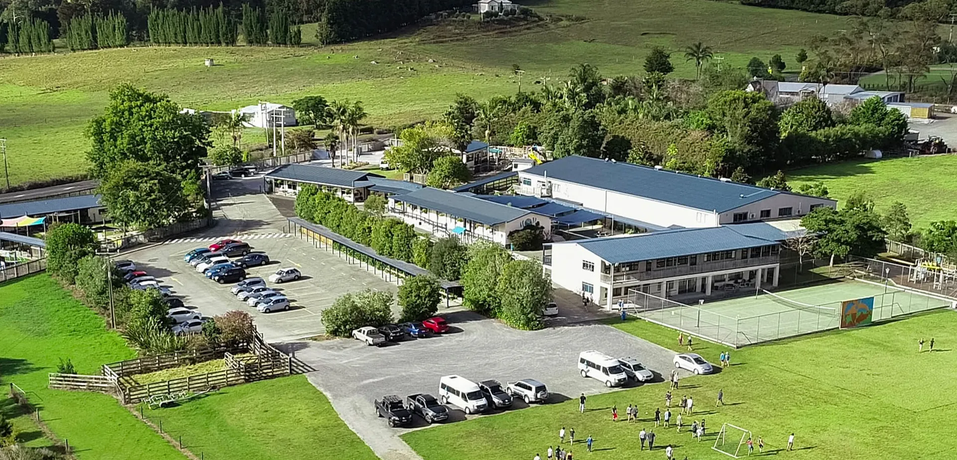 Il campus della Springbank School mostra diversi edifici, parcheggi con veicoli e colline verdi sullo sfondo.