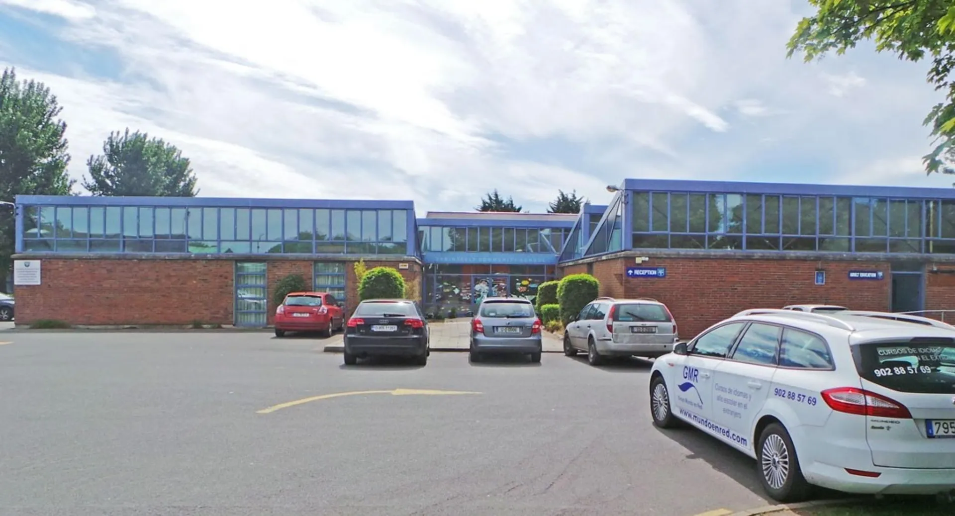 L'edificio in mattoni rossi della Cabinteely Community School con ampie vetrate blu e auto parcheggiate davanti.