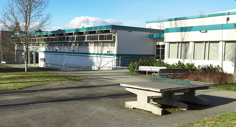 L'edificio moderno a più piani della Cariboo Hill School è circondato da un'area pavimentata con una panchina in cemento.
