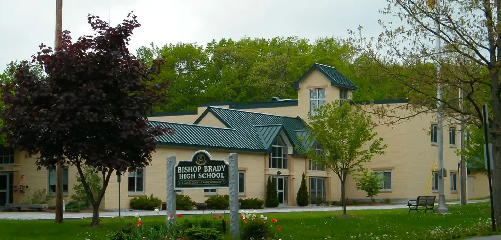 L'edificio in mattoni a due piani con il tetto in metallo verde appartiene alla Bishop Brady High School ed è circondato da alberi e un prato.