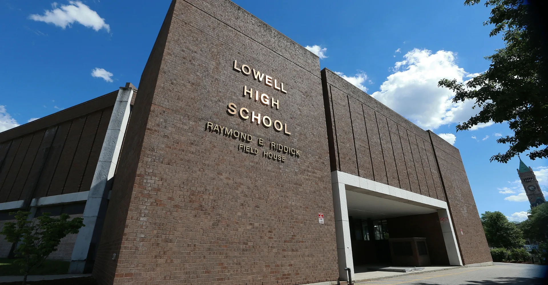 L'edificio in mattoni della Lowell High School si trova davanti a un cielo blu con qualche nuvola sparsa.