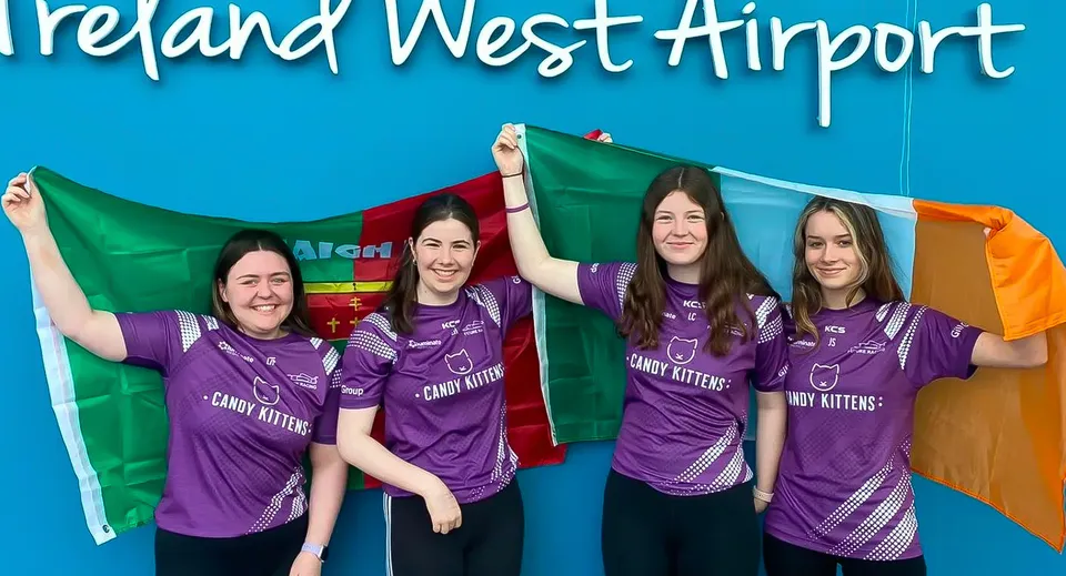 Quattro studentesse della St. Mary’s Secondary indossano t-shirt viola dei Crazy Kittens davanti al cartello Ireland West Airport.