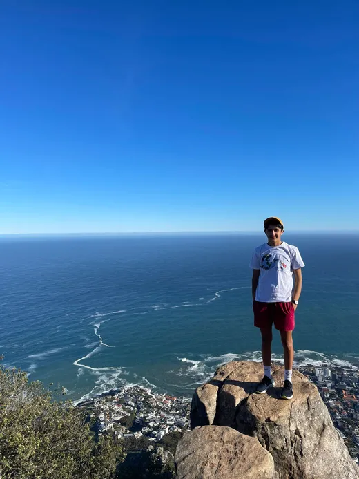 Studente in piedi su una vetta rocciosa sopra l'oceano e la costa di Città del Capo