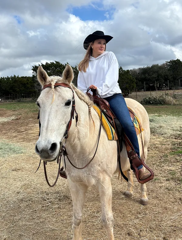Chica con sombrero de vaquero montando un caballo claro en un rancho