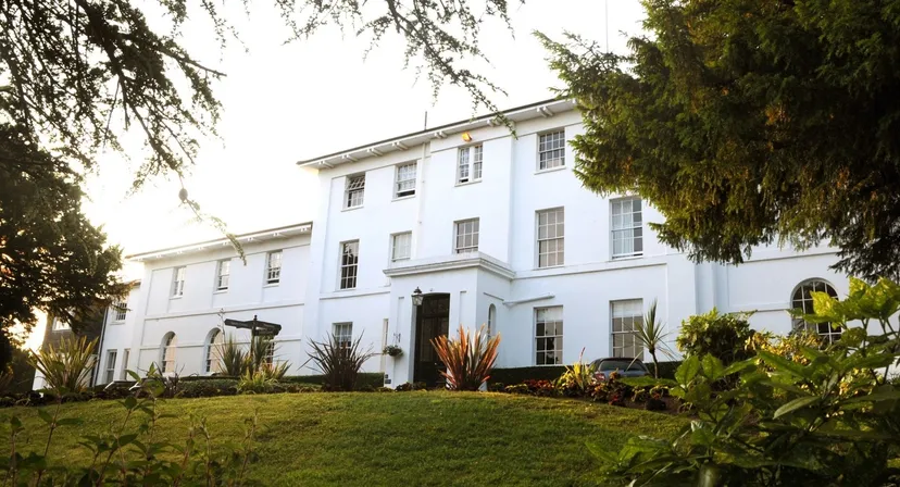 L'edificio principale bianco della Sidcot School si trova davanti a un prato ben curato ed è circondato da alberi alti.
