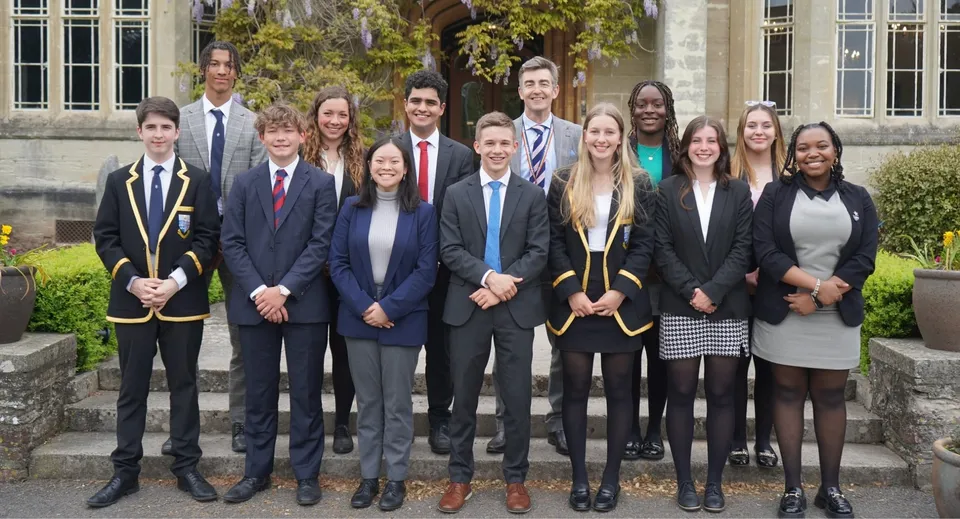 Un gruppo di studenti in abito formale posa sulla scalinata davanti a un edificio del campus del Queen’s College.