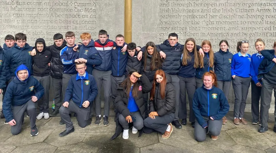Un gruppo di studenti davanti a una parete con una scritta nel campus della Patrician Presentation Secondary School.