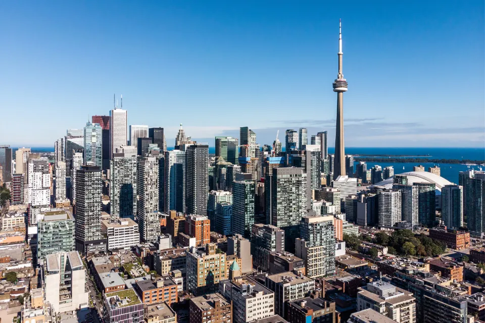 Un ampio skyline cittadino con grattacieli e una caratteristica torre delle telecomunicazioni sotto un cielo limpido vicino alla École secondaire publique Carrefour Jeunesse.