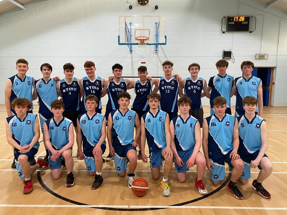 Un gruppo di studenti del St. Michael's College posa nella palestra davanti a un canestro da basket.