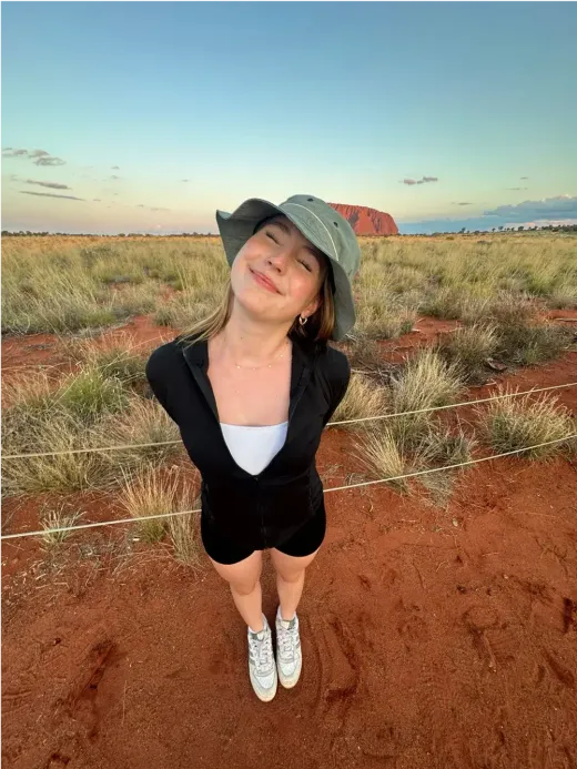 Alicia lächelt mit Hut im australischen Outback, im Hintergrund der Uluru
