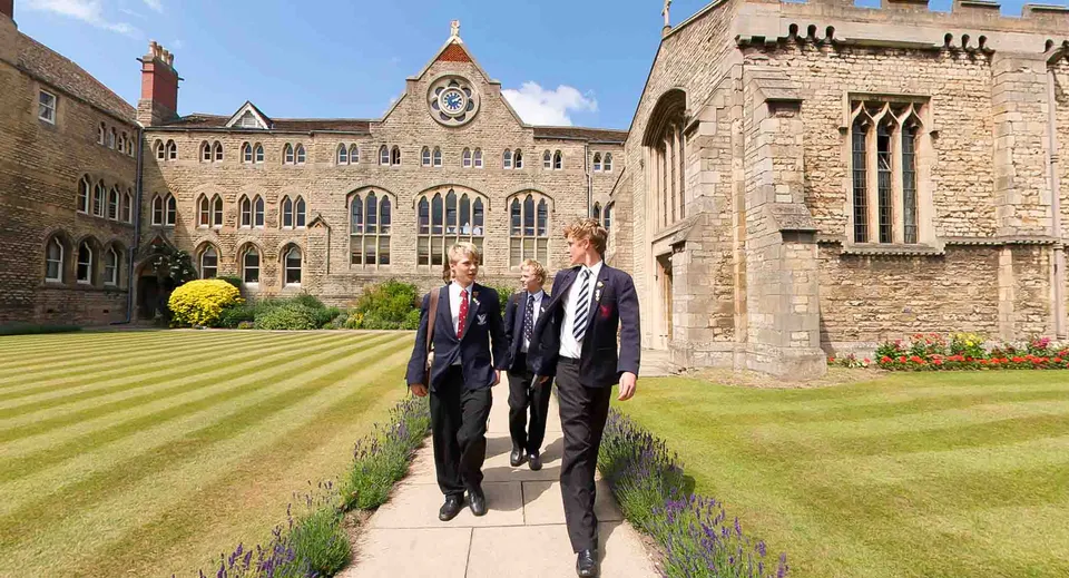 Tre studenti della Stamford Endowed Schools in divisa scolastica camminano su un vialetto davanti agli edifici storici in pietra.