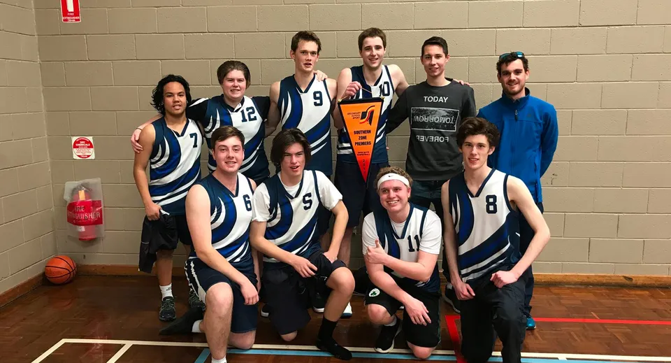Un gruppo di studenti e studentesse del Hamilton Secondary College in posa come squadra di basket nella palestra.