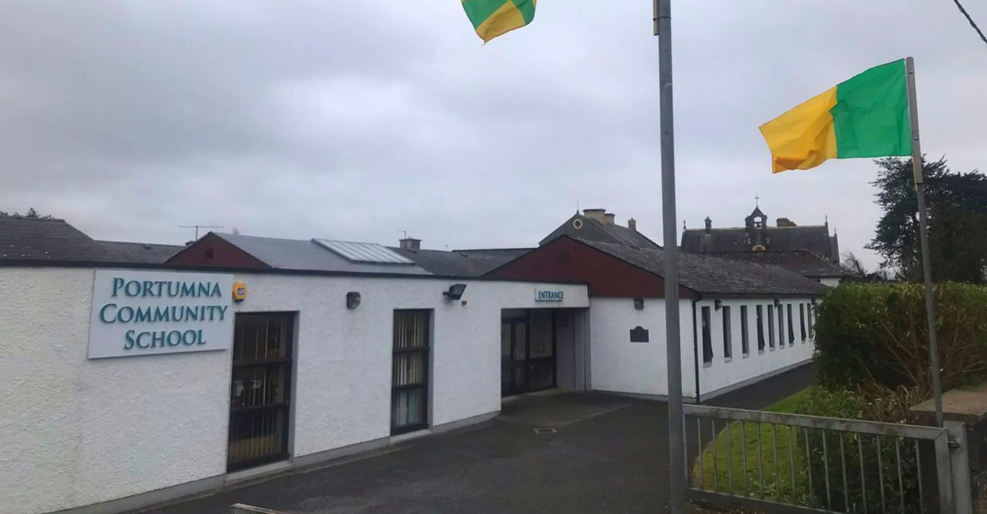 L'edificio della Portumna Community School con l'ingresso principale, l'insegna della scuola e due bandiere.