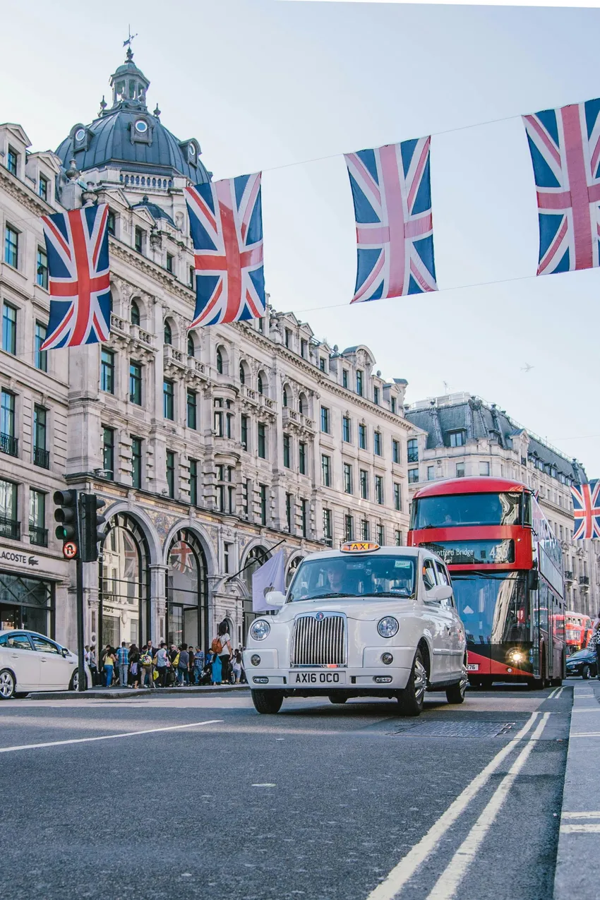 Strada di Londra con taxi nero, autobus a due piani e bandierine dell'Union Jack