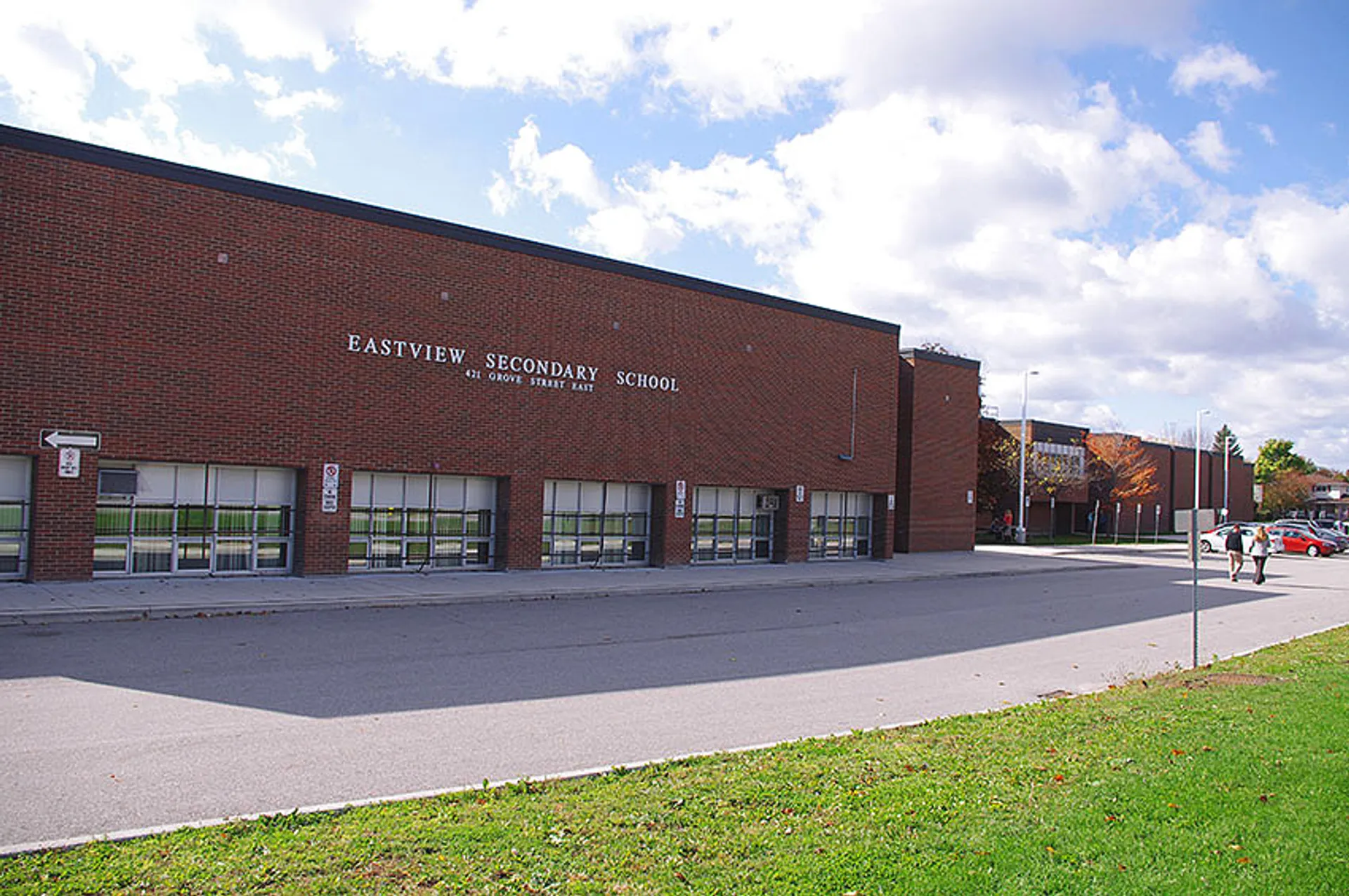 Il grande edificio in mattoni della Eastview Secondary School davanti a un cielo nuvoloso con un'area pavimentata e un prato.
