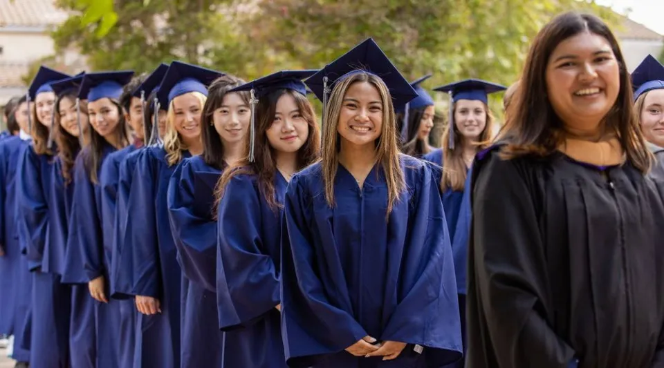 Studentesse della Villanova Preparatory School in piedi con toghe di laurea blu davanti ad alberi e sfondo verde.