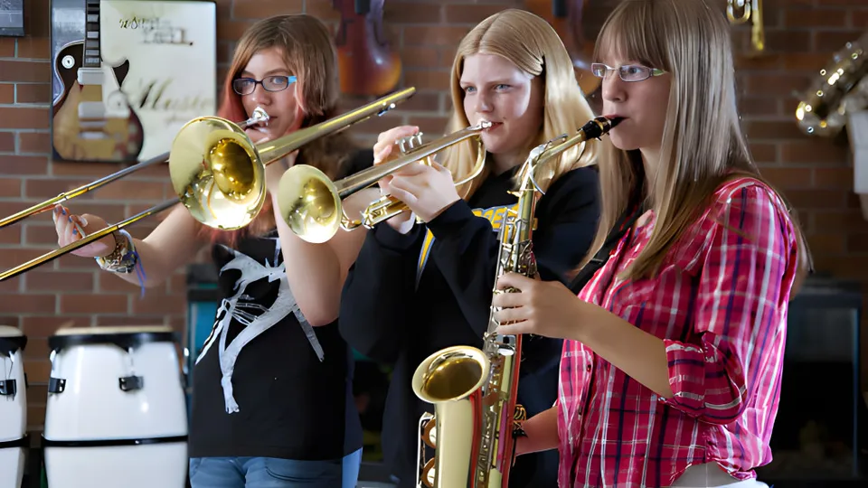 Tre studentesse della École J.E. Lapointe School suonano insieme strumenti a fiato in ottone in una stanza con pareti in mattoni.